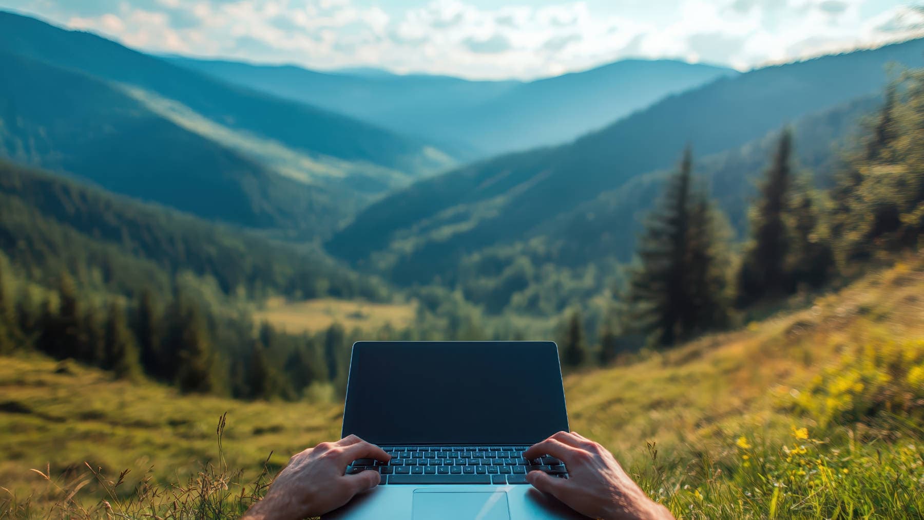 Hands on laptop against mountain valley - merging digital craftsmanship with natural inspiration at Spire Forge.